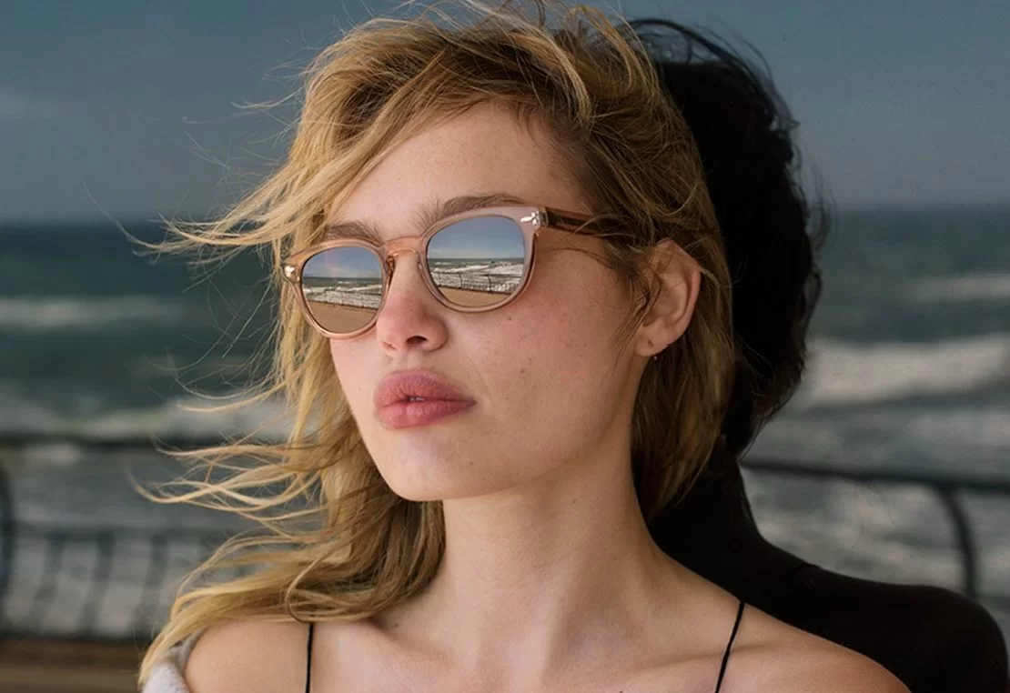 Brillenmarke Oliver Peoples - Frau vor Glas mit Sonnenbrille