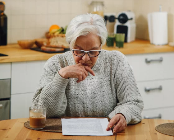 Lesebrillen - Ältere Frau mit weißem Haar liest auf in Küche