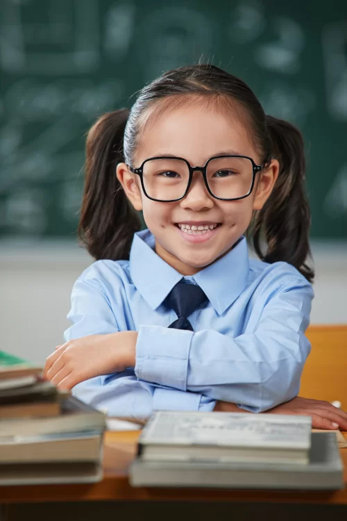 Kinderbrillen bei Sattler Optik - Kleines Mädchen in Schuluniform und mit Zöpfen trägt Kinderbrille und lacht