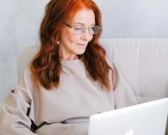 Lesebrillen bei Sattler Optik - Ältere Frau mit roten Haaren arbeitet auf Laptop mit Lesebrille