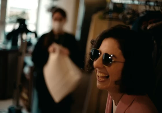 Lazare Studios Brillen - Frau mit dunklen Haaren und rosa Sakko lacht und trägt eine Sonnenbrille