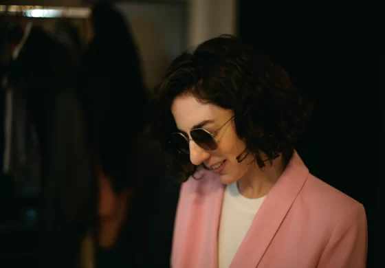 Lazare Studios Brillen - Frau mit dunklen Haaren und rosa Sakko mit Sonnenbrille