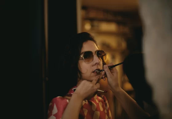 Lazare Studios Brillen - Frau mit dunklen Haaren trägt Sonnenbrille und wird geschminkt