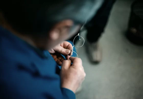 Lazare Studios Brillen - Mann arbeitet an Brillenfassung in blauem Arbeitsmantel