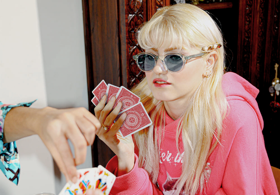 Peter and May Brillen - Frau mit blonden Haaren und Sonnenbrille spielt Karten an Tisch